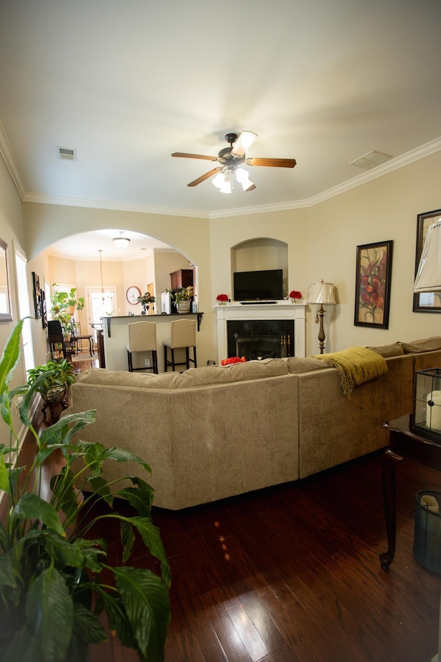 living room with crown molding, a ceiling fan, arched walkways, dark wood-type flooring, and visible vents