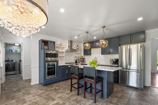 kitchen featuring wine cooler, wall chimney range hood, light countertops, appliances with stainless steel finishes, and washer / dryer