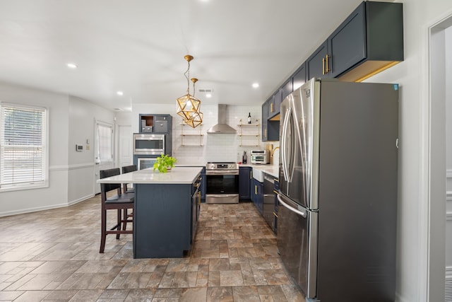kitchen featuring wall chimney exhaust hood, decorative backsplash, stone finish floor, light countertops, and appliances with stainless steel finishes