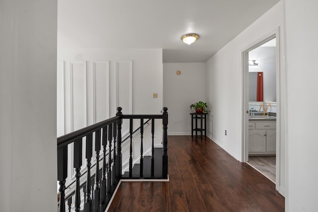 hallway with dark wood finished floors, baseboards, an upstairs landing, and a sink
