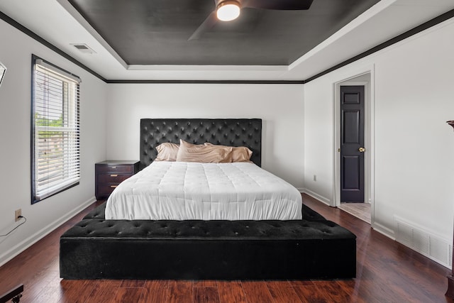bedroom with a tray ceiling, wood finished floors, visible vents, a ceiling fan, and baseboards