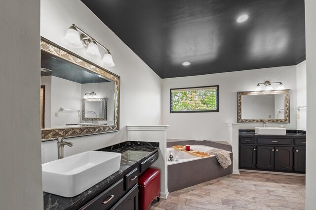full bath featuring two vanities, wood finished floors, a garden tub, and a sink