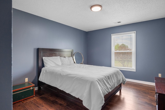 bedroom with baseboards, wood finished floors, visible vents, and a textured ceiling
