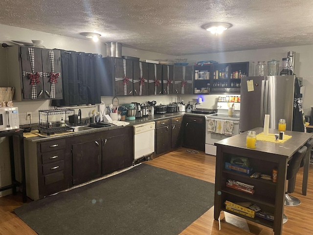kitchen with dark countertops, wood finished floors, a textured ceiling, and white appliances