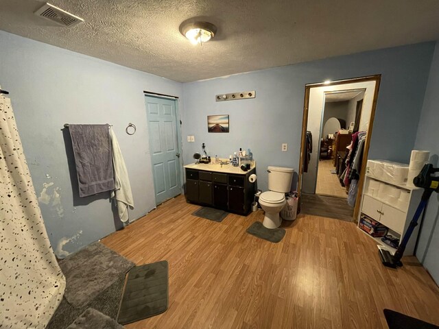 bathroom with wood finished floors, visible vents, toilet, vanity, and a textured ceiling