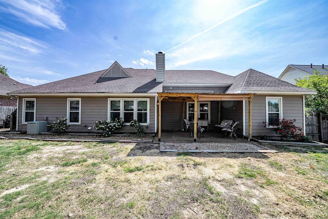 rear view of property with central air condition unit, a chimney, fence, a patio area, and a shingled roof