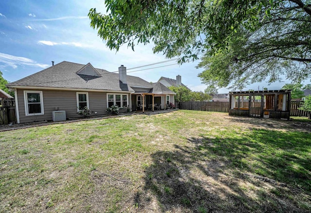 back of property with a fenced backyard, central AC unit, roof with shingles, and a lawn