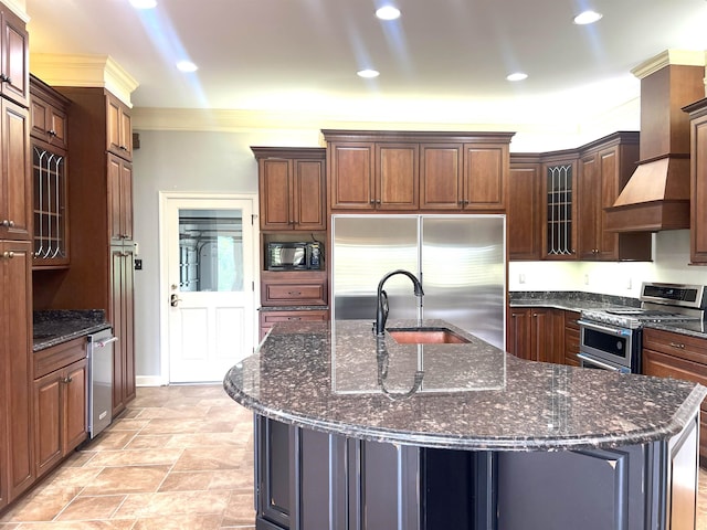 kitchen with a center island with sink, a sink, dark stone countertops, glass insert cabinets, and built in appliances