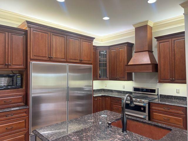 kitchen with dark stone counters, stainless steel appliances, custom exhaust hood, and ornamental molding