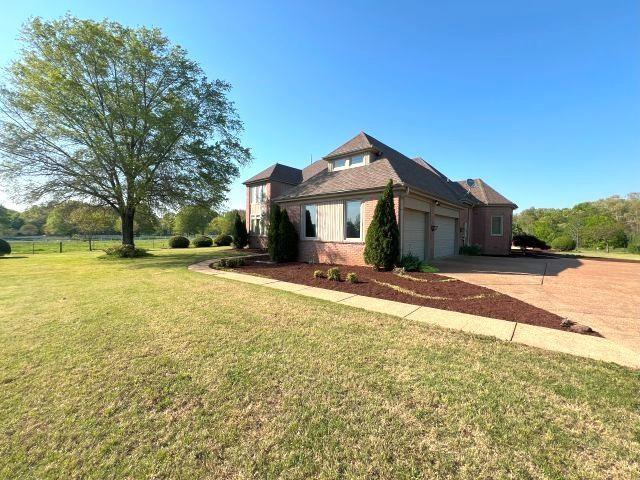 view of side of home with fence, an attached garage, brick siding, concrete driveway, and a lawn