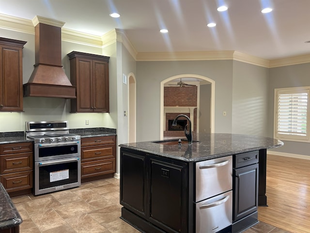 kitchen with appliances with stainless steel finishes, a sink, a brick fireplace, arched walkways, and custom exhaust hood