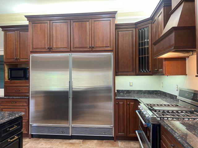 kitchen with stainless steel appliances, glass insert cabinets, custom range hood, and dark stone countertops