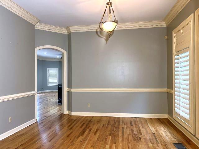 spare room with arched walkways, ornamental molding, baseboards, and wood finished floors