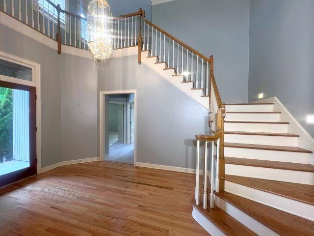 stairs with baseboards, an inviting chandelier, wood finished floors, and a towering ceiling