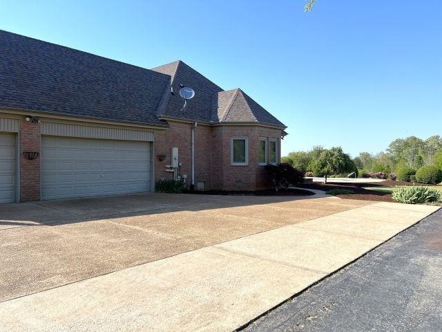 view of front of property featuring brick siding, an attached garage, driveway, and a shingled roof