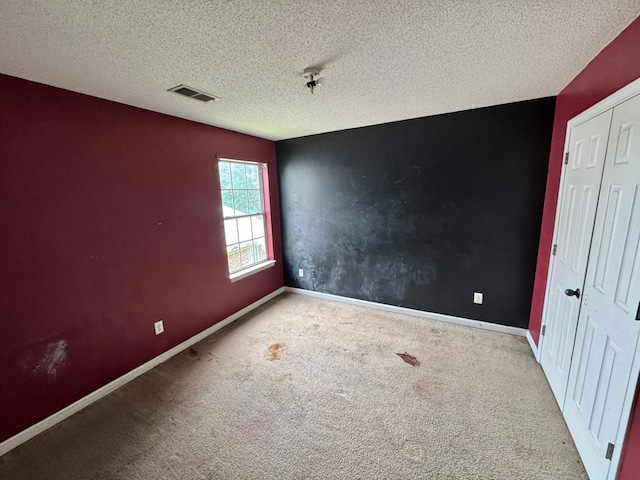 carpeted spare room featuring baseboards, visible vents, and a textured ceiling