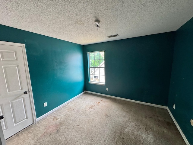 carpeted empty room featuring baseboards, visible vents, and a textured ceiling