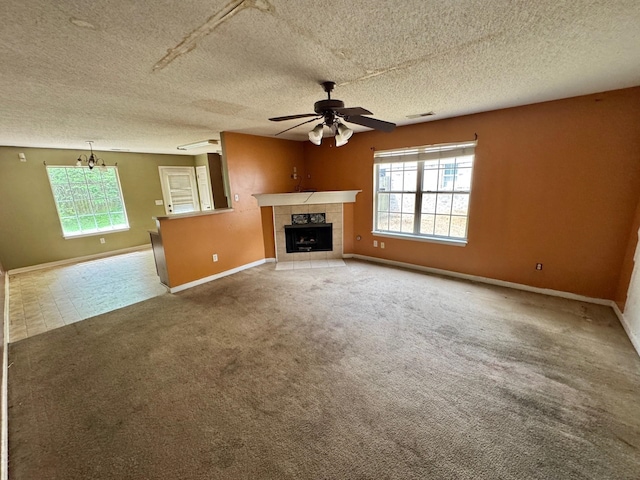 unfurnished living room with a textured ceiling, ceiling fan, a tiled fireplace, baseboards, and carpet flooring