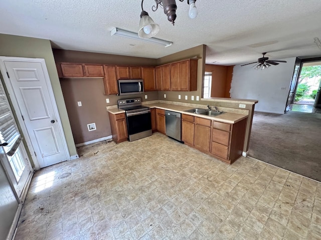 kitchen with stainless steel appliances, a peninsula, a sink, baseboards, and brown cabinetry