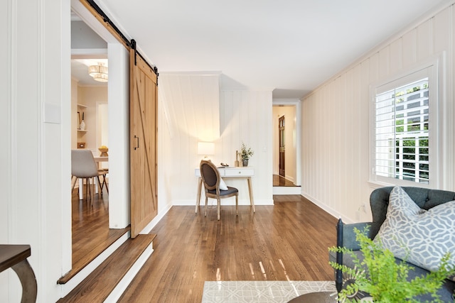 sitting room with a barn door, baseboards, ornamental molding, and wood finished floors