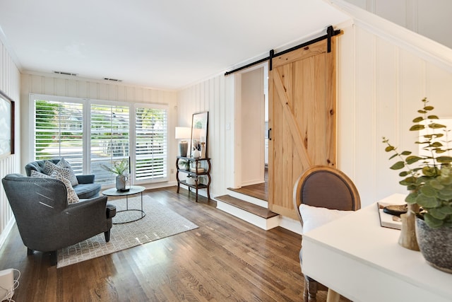living room featuring a decorative wall, dark wood finished floors, ornamental molding, and a barn door