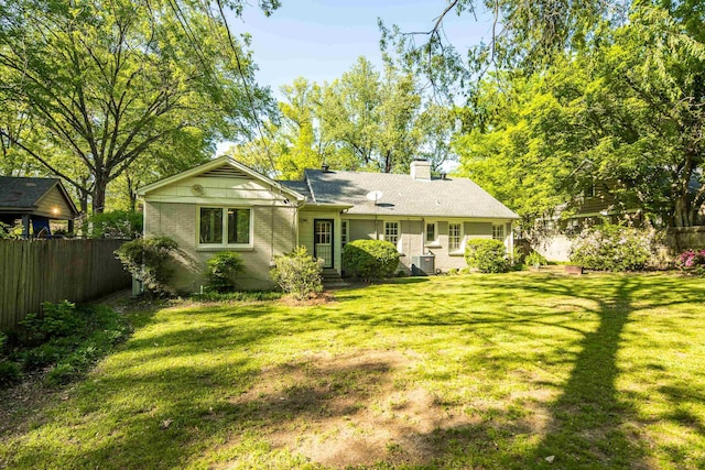 rear view of house featuring a lawn, fence, a chimney, and brick siding