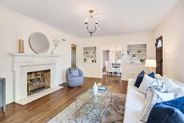 living area featuring wood finished floors, arched walkways, a premium fireplace, built in shelves, and a notable chandelier