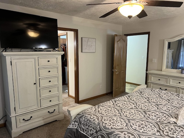 bedroom with a walk in closet, baseboards, a textured ceiling, and light colored carpet