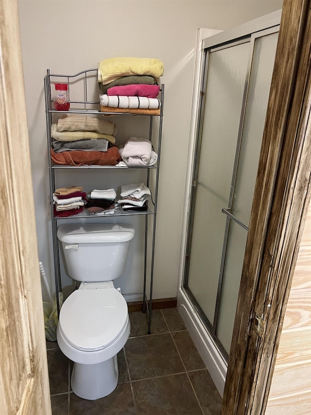 bathroom featuring baseboards, toilet, and a stall shower