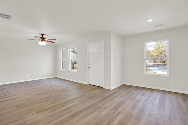 unfurnished living room with baseboards, wood finished floors, visible vents, and a healthy amount of sunlight