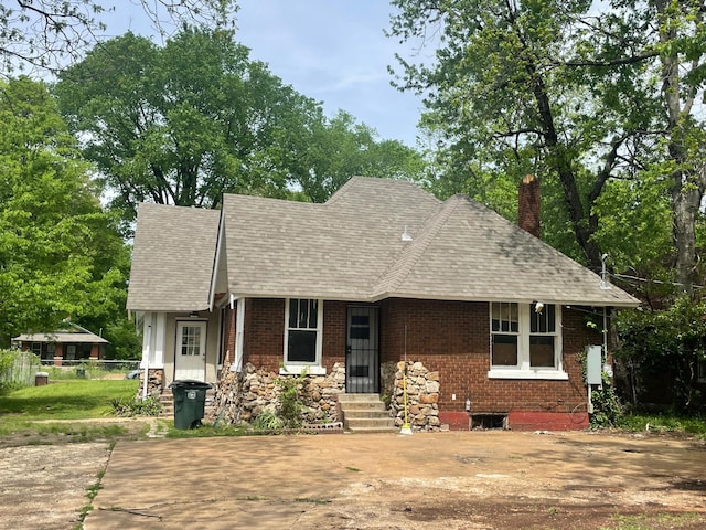 view of front of home featuring fence, a shingled roof, a chimney, and brick siding