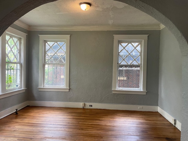 interior space featuring a textured wall, wood finished floors, arched walkways, and ornamental molding