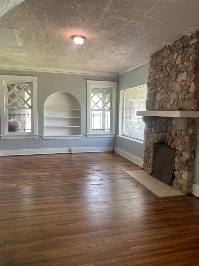 unfurnished living room with a textured ceiling, baseboards, built in features, a stone fireplace, and wood-type flooring