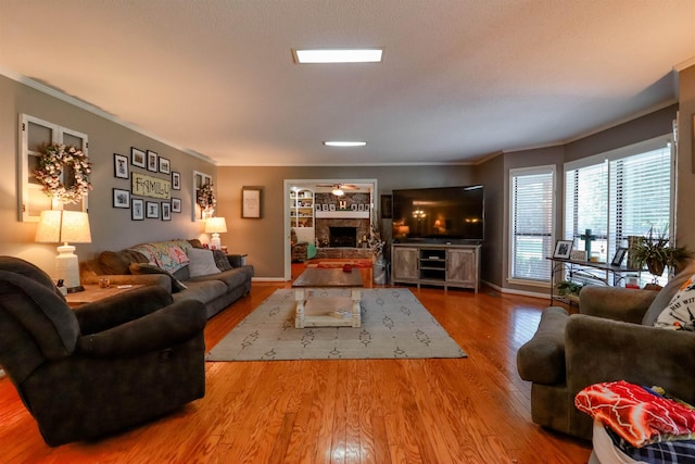 living area featuring wood finished floors, crown molding, baseboards, and a stone fireplace