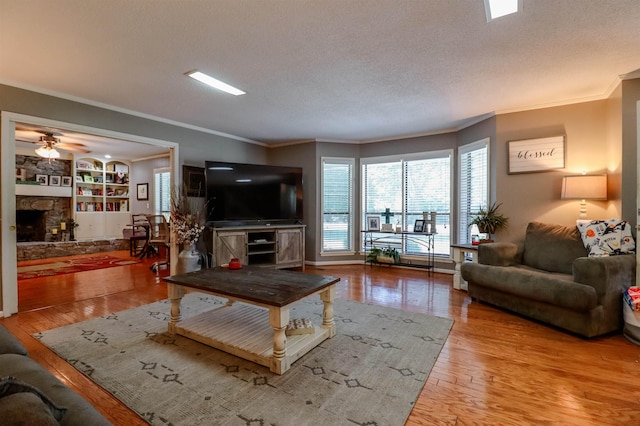 living room featuring wood finished floors, a stone fireplace, a textured ceiling, and ornamental molding