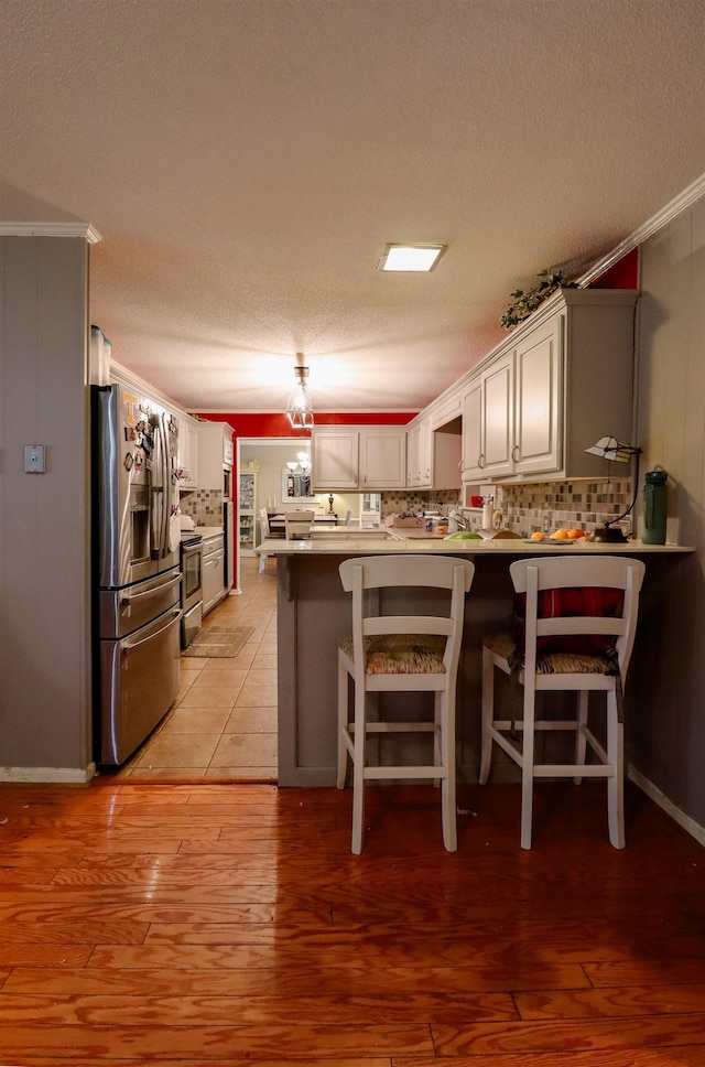 kitchen with a peninsula, backsplash, light wood-style floors, and stainless steel appliances