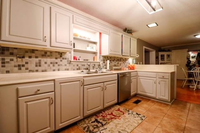 kitchen with light countertops, stainless steel dishwasher, a sink, decorative backsplash, and a peninsula