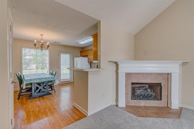 living area featuring light wood-type flooring, baseboards, a chandelier, a tiled fireplace, and a textured ceiling