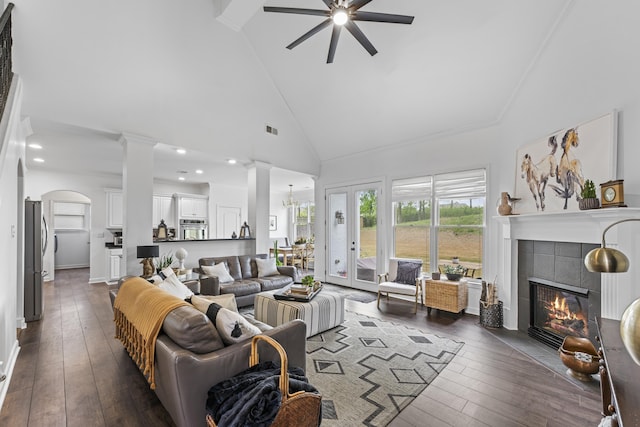 living room featuring a tiled fireplace, decorative columns, ceiling fan, high vaulted ceiling, and dark wood-type flooring