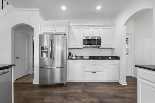 kitchen with arched walkways, dark countertops, appliances with stainless steel finishes, and crown molding
