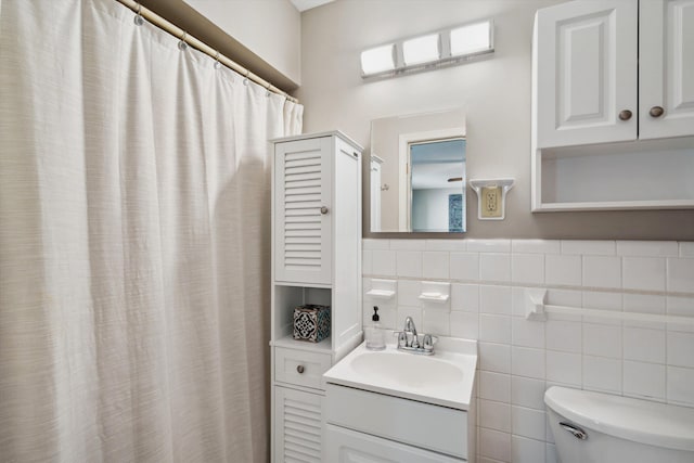full bathroom with toilet, vanity, a wainscoted wall, and tile walls