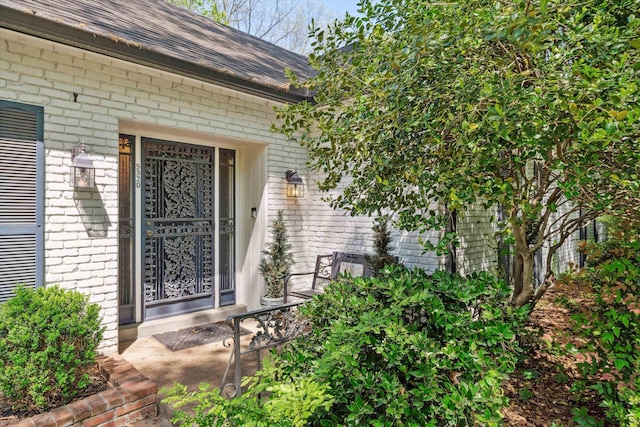 entrance to property with brick siding and a shingled roof