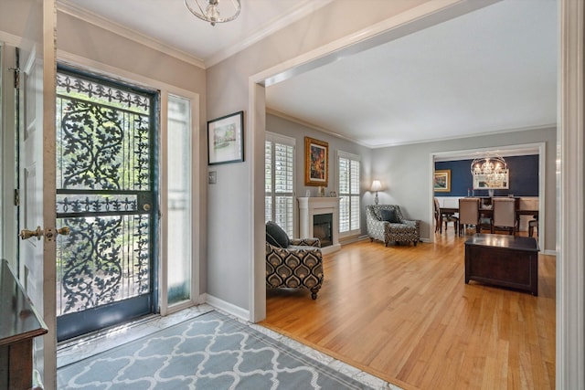 foyer entrance with crown molding, wood finished floors, a fireplace, baseboards, and a notable chandelier