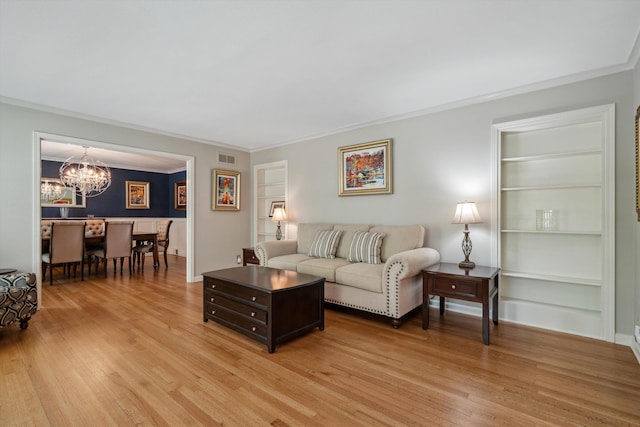 living room with built in shelves, crown molding, a chandelier, and light wood-style flooring