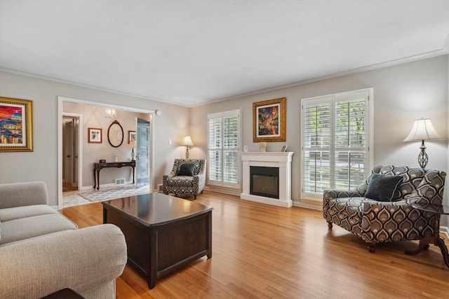 living room with baseboards, ornamental molding, a glass covered fireplace, and light wood-style floors