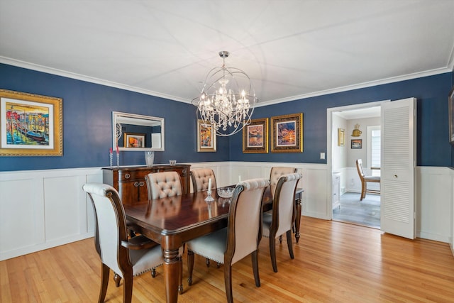 dining room featuring a wainscoted wall, ornamental molding, a decorative wall, a chandelier, and light wood-style flooring