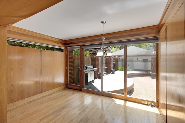 unfurnished dining area with wooden walls, wood finished floors, and a notable chandelier