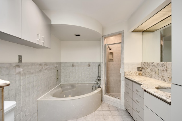 full bath with a shower stall, a tub with jets, tile patterned floors, vanity, and tile walls