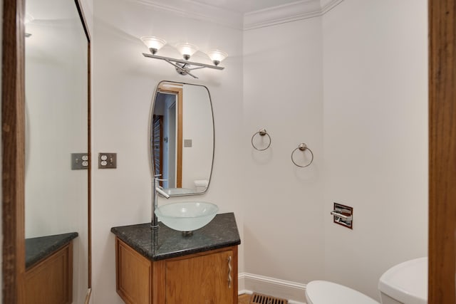 half bathroom featuring toilet, visible vents, baseboards, vanity, and ornamental molding