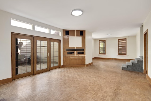 unfurnished living room featuring baseboards, french doors, and a wealth of natural light